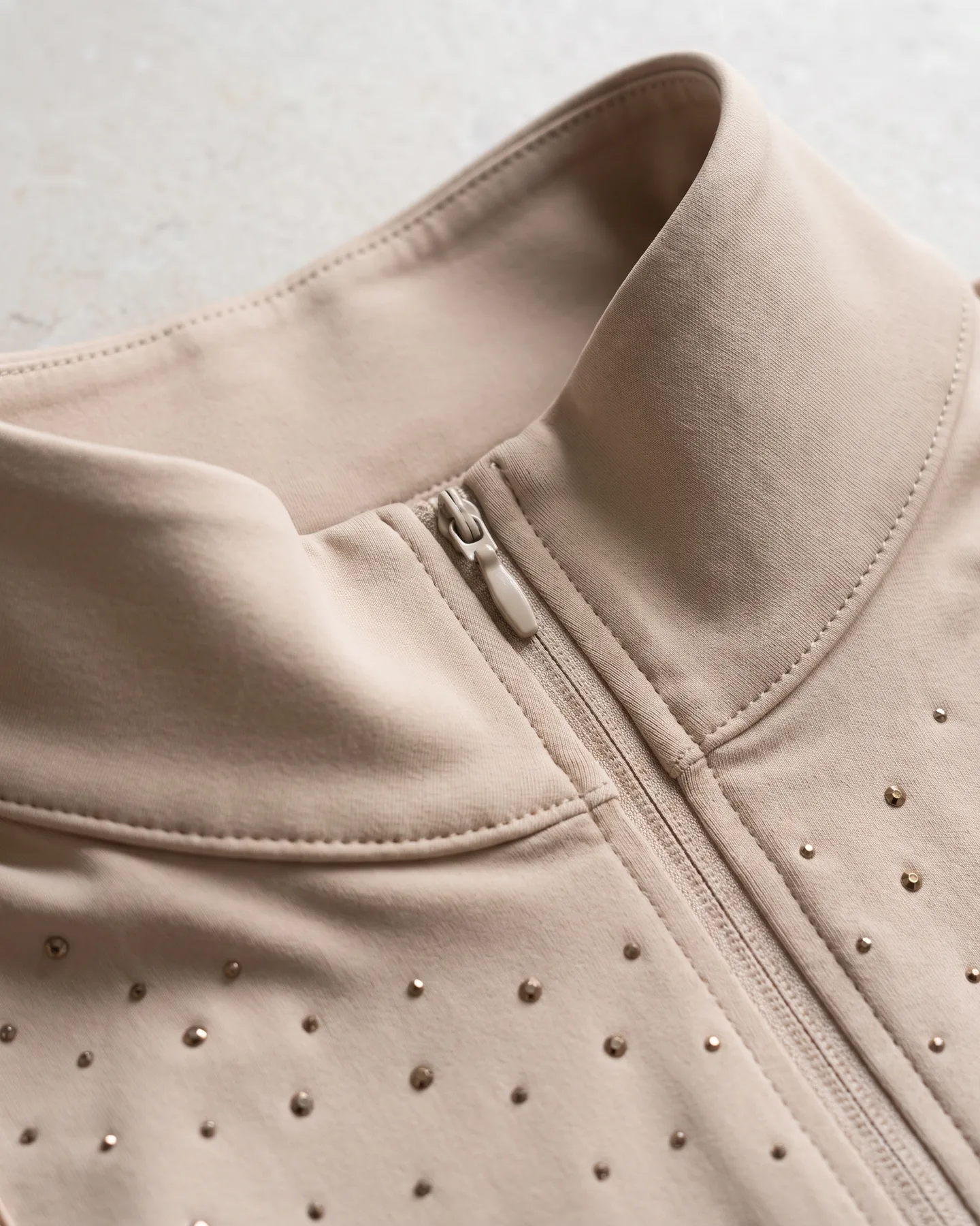 Col montant sable d’une chemise de concours, zip court et premiers strass sous l’encolure