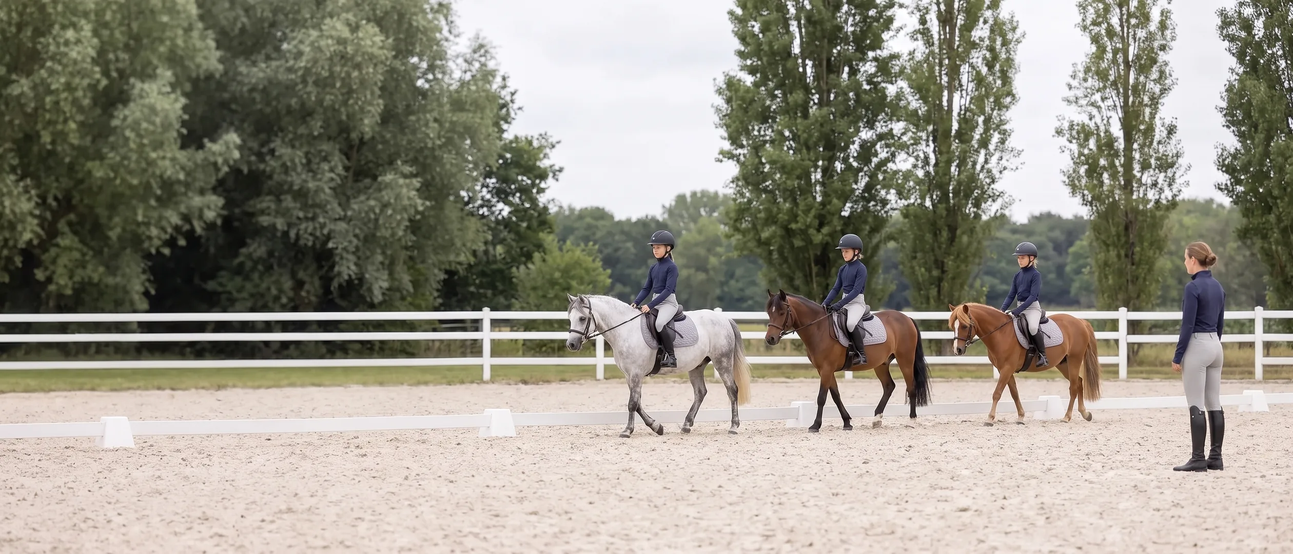 Leçon d’équitation en carrière : trois jeunes cavaliers sur leurs poneys et leur monitrice