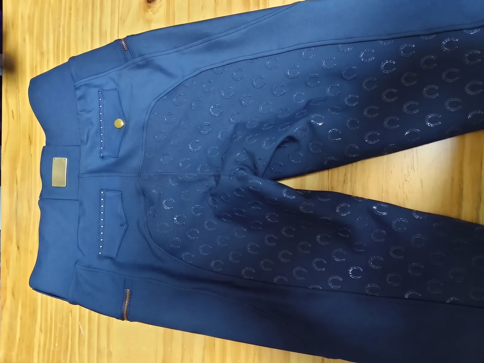 Pantalon d’équitation marine posé à plat, grip intégral à motif et plaque métal à la ceinture