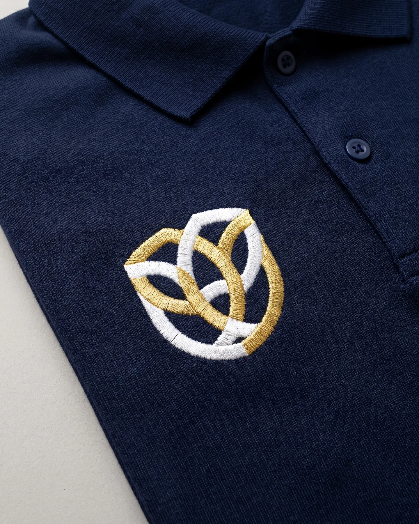 Logo brodé en fil blanc et doré sur un polo d’équitation personnalisé marine, près de la patte boutonnée