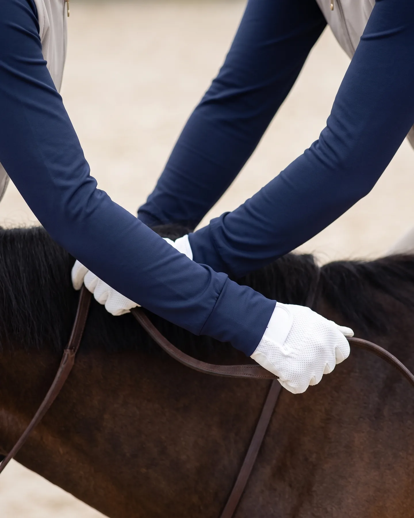 Mains gantées sur les rênes, poignets couverts par les manches marine d’un sous-pull d’équitation